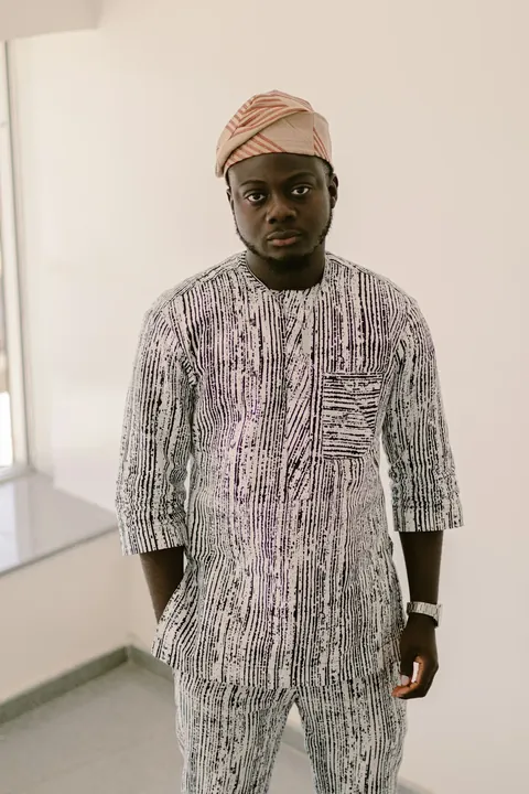 A man in a hand dyed striped two piece and woven cap, hands in his pockets