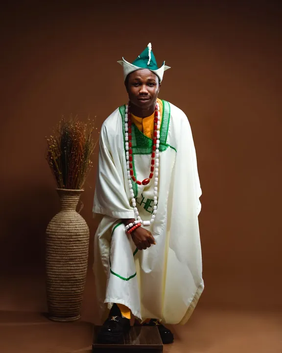 A man seated in an ivory agbada with green trim and coral beads