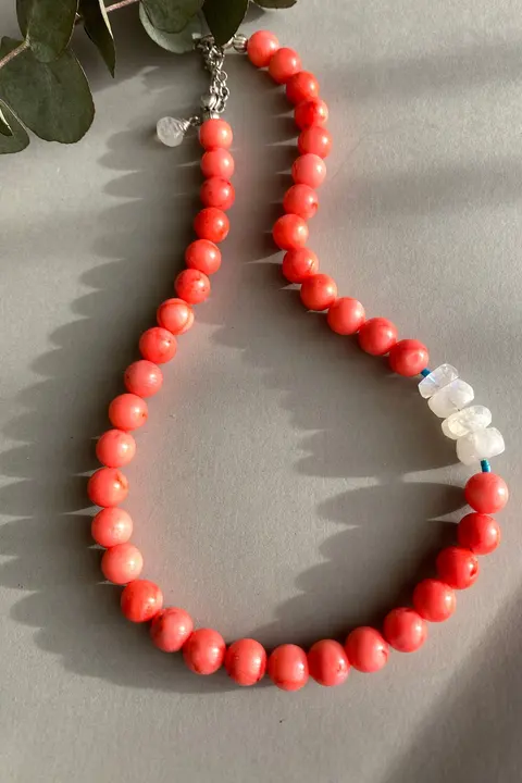A strand of coral red beads with three clear stones, laid on a pale surface