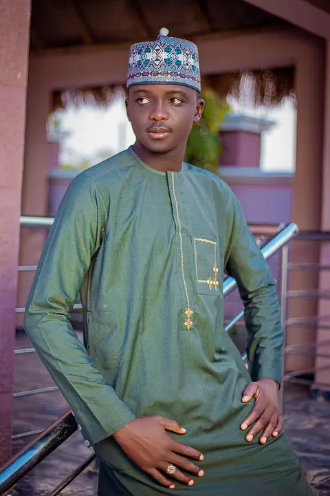 A man in a deep green kaftan with a fine embroidered pocket, leaning on a rail