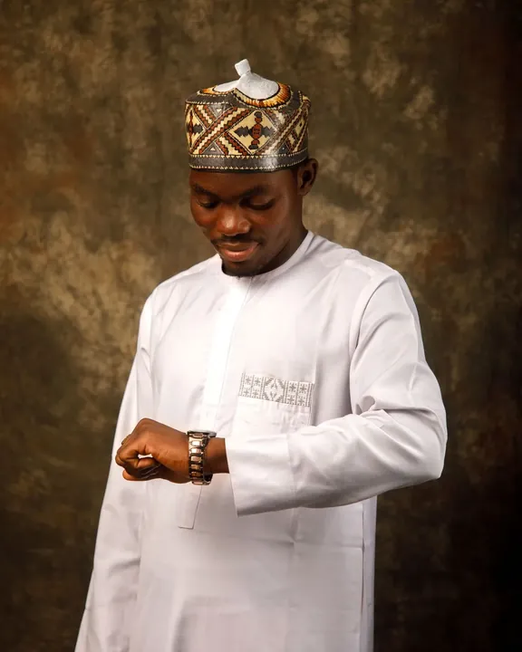 A man in an ivory senator top with a woven chest panel, glancing at his watch