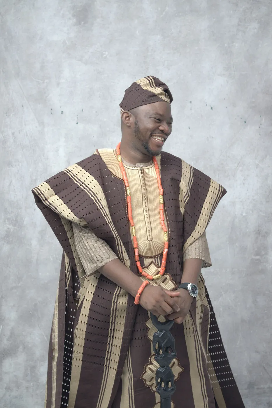 A man in a brown and cream striped aso oke agbada with coral beads