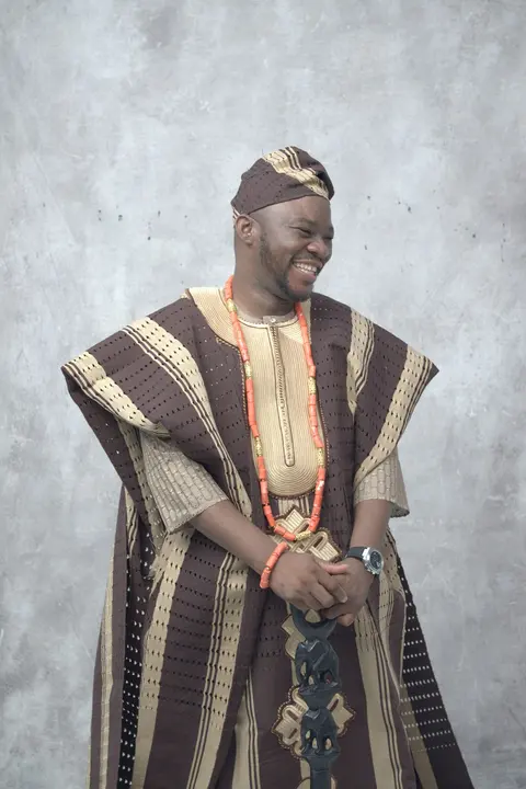 A man laughing in a brown and cream striped aso oke agbada with coral beads