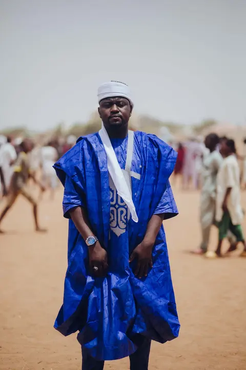 A man in a royal blue babban riga with dense tonal embroidery, a white scarf at his neck