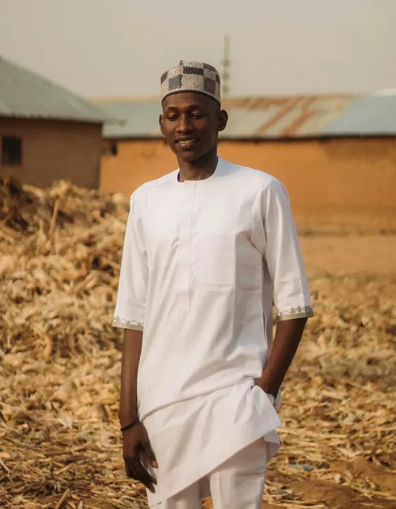 A man in a white short sleeved tunic and matching trousers standing outdoors