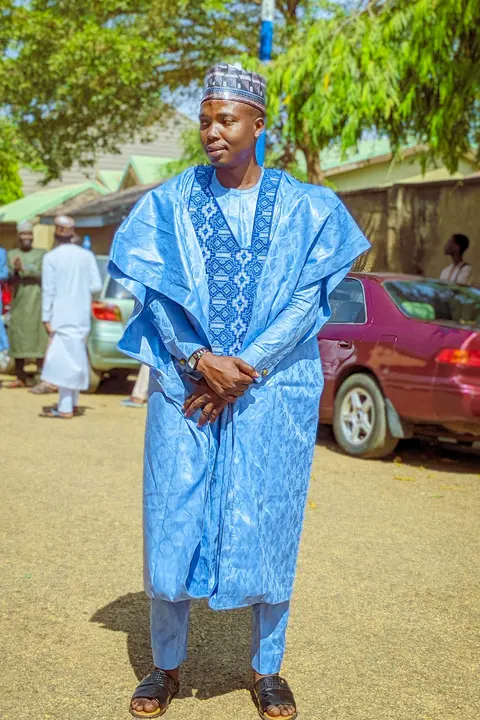 A man in a sky blue agbada with navy embroidery down the front