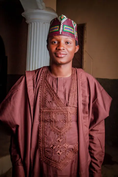 A man in a wine agbada with matching geometric embroidery and a woven cap