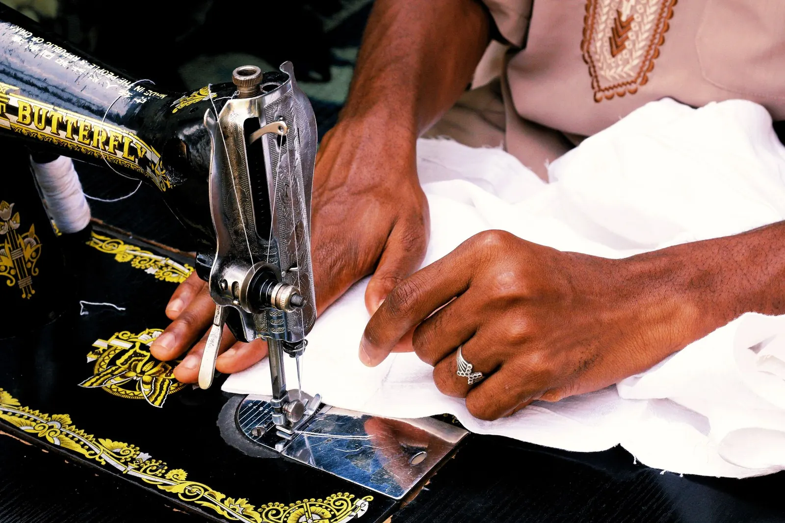 A tailor's hands guiding white fabric under the needle of a sewing machine