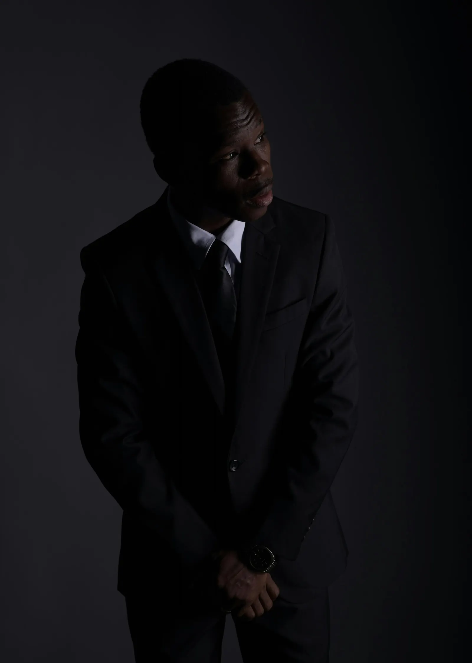 A man in a black suit standing in deep shadow